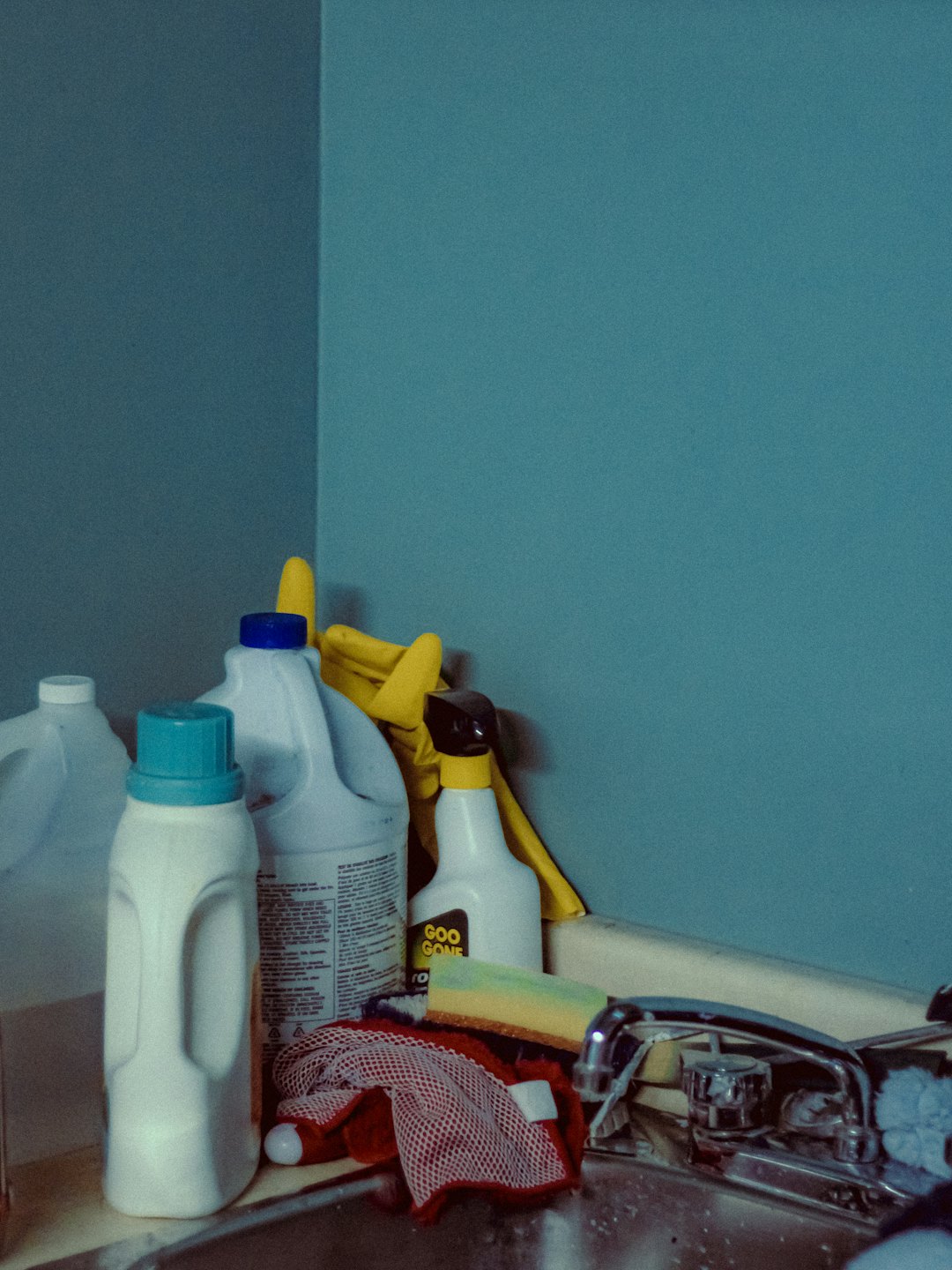 Cleaning supplies and sponges sit on a kitchen countertop.
