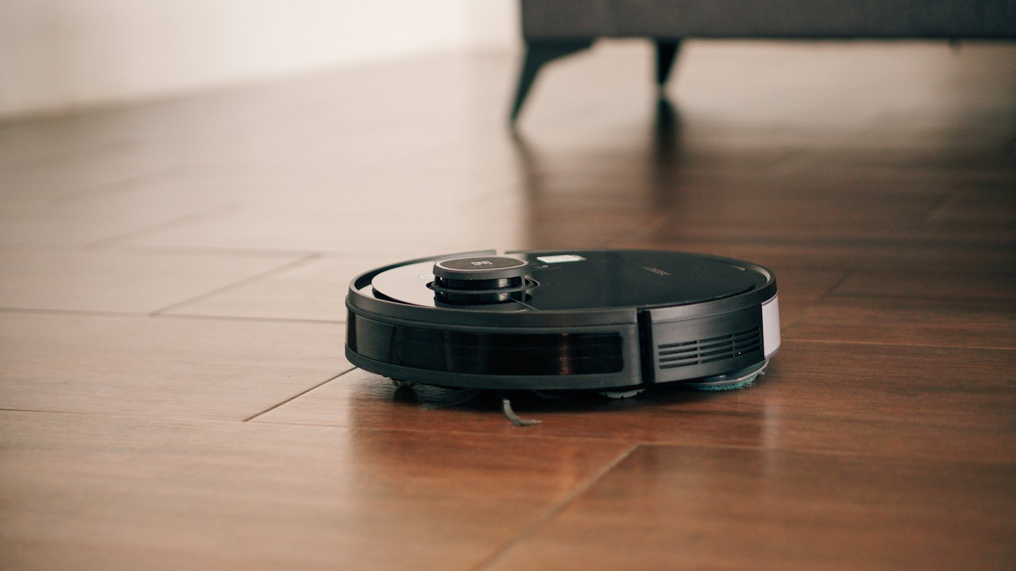 Black robotic vacuum cleaner moving across a wooden floor.