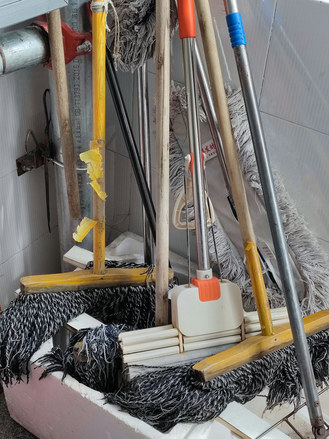 A collection of mops and brooms stored against a tiled wall.